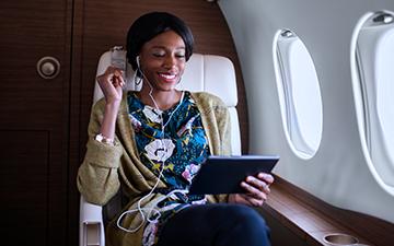 黑头发，花衬衫的女人坐着私人飞机, 戴着与平板电脑相连的耳机